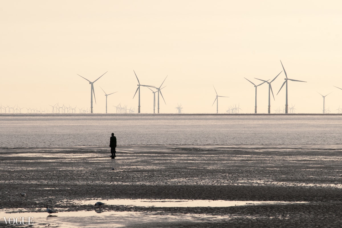 A lone figure on a beach beneath a line of offshore wind turbines, photographed by Emanuele Zanchettin
